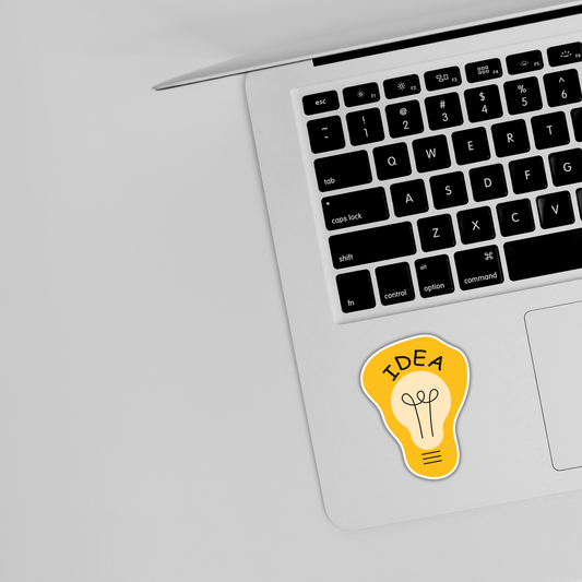 Yellow idea lightbulb sticker on laptop by keyboard, cute trendy sticker design
